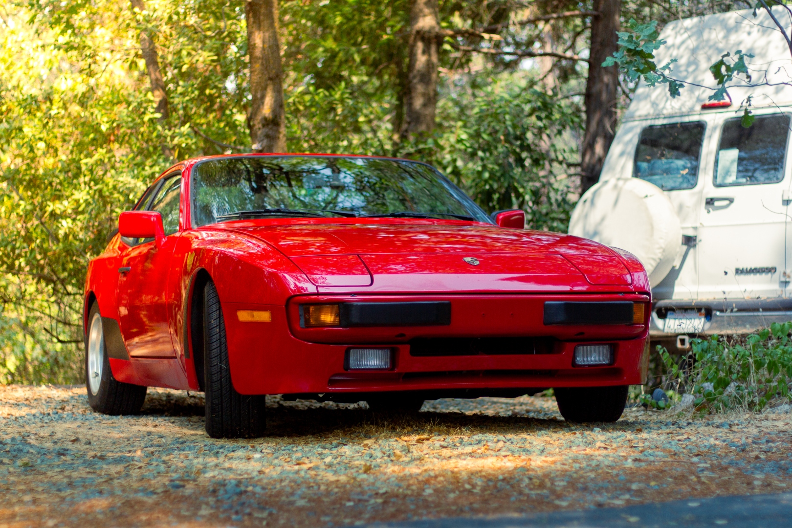 Red Porsche 944 front three-quarter in dappled forest light