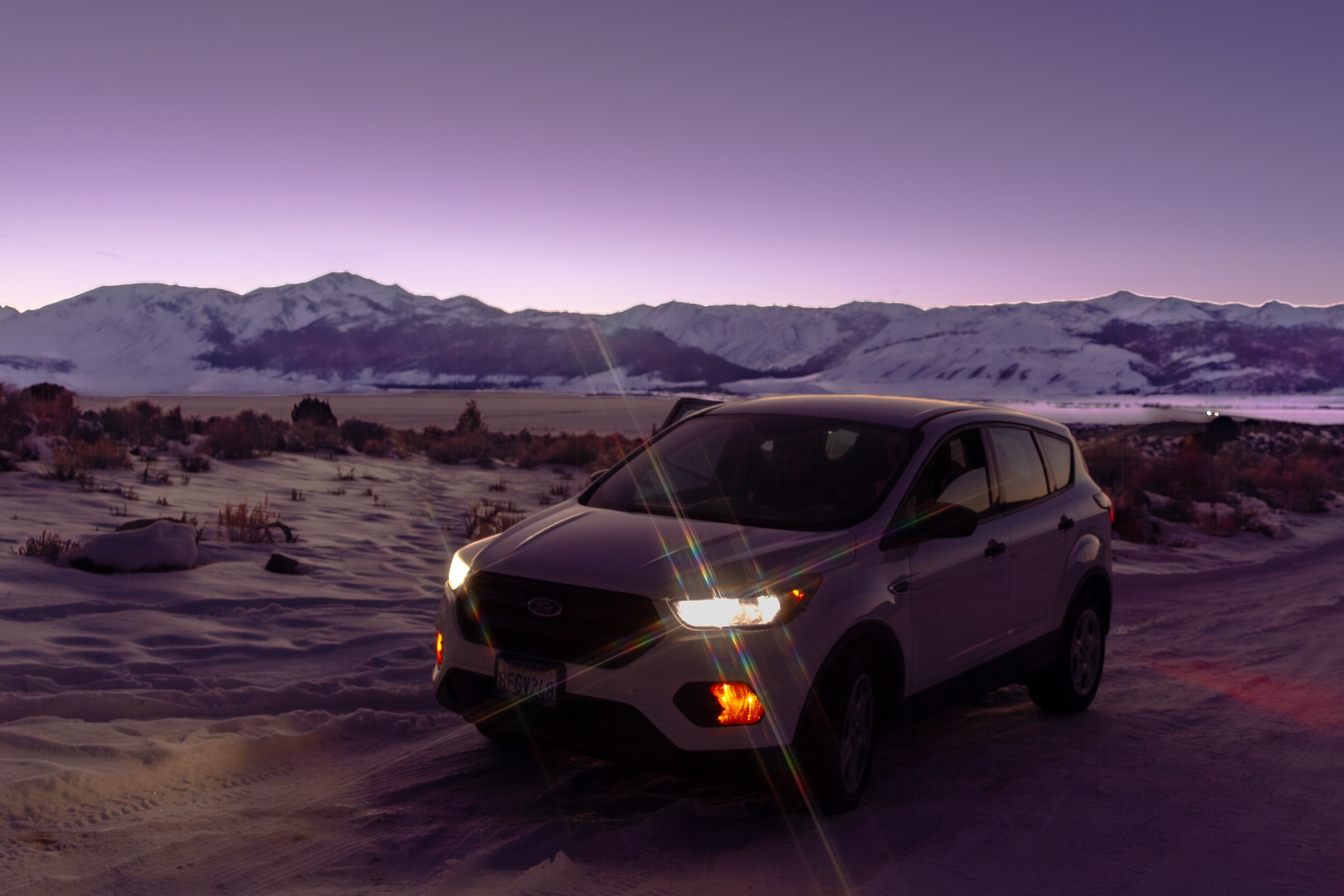Ford Escape with headlight lens flare parked in snowy Sierra Nevada landscape at dusk
