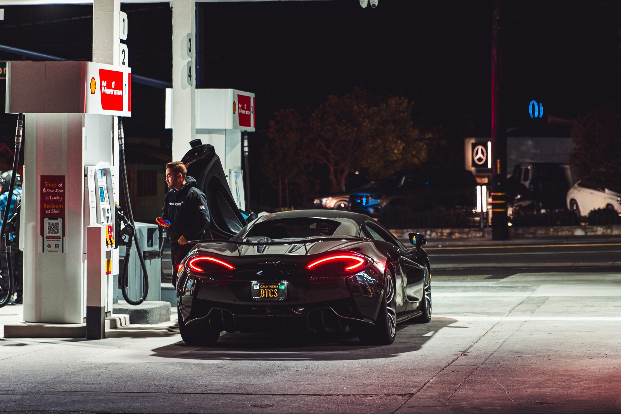 Black McLaren 570S at Shell station at night, dihedral door open