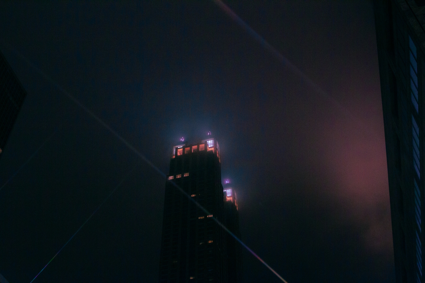 NYC skyscraper at night through fog with laser light streaks