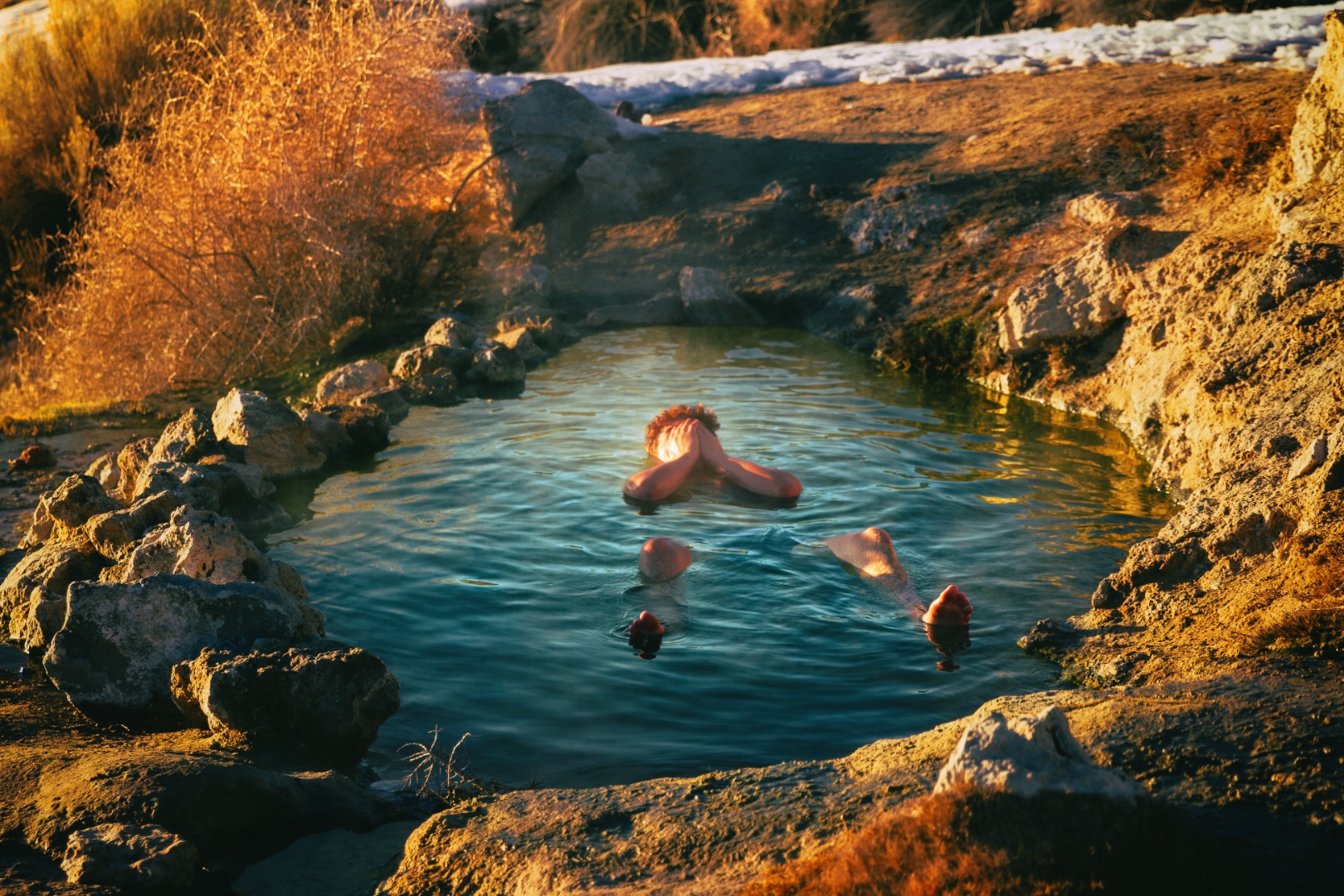 Person floating in natural hot spring pool surrounded by desert landscape