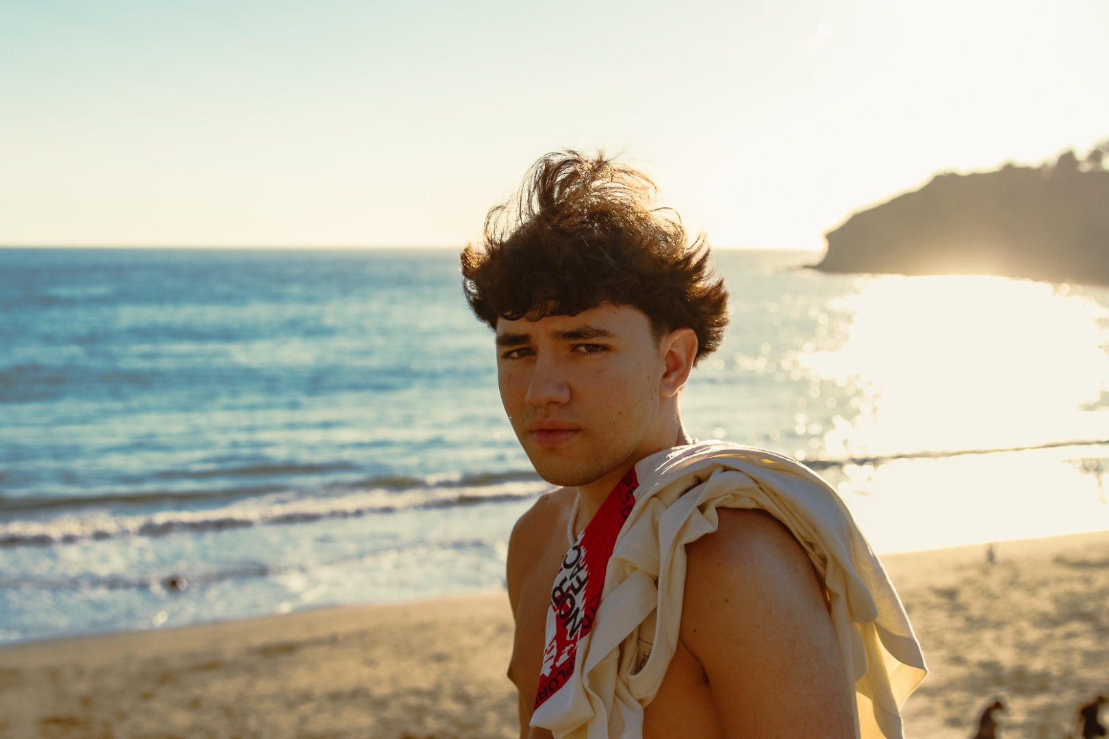 Young man looking back over shoulder on California beach at golden hour