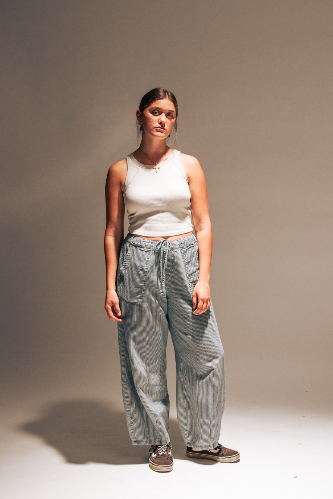 Woman in white tank and wide-leg cords standing against neutral studio backdrop