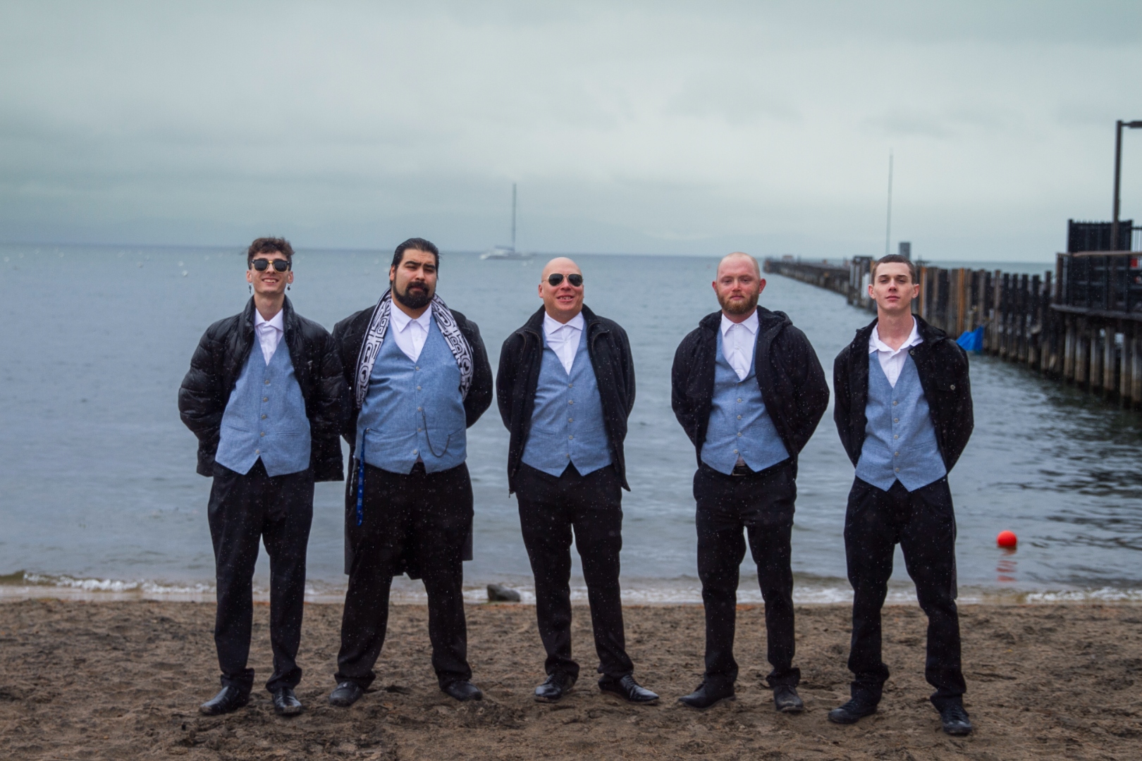 Groomsmen in formal wear standing on beach in overcast light