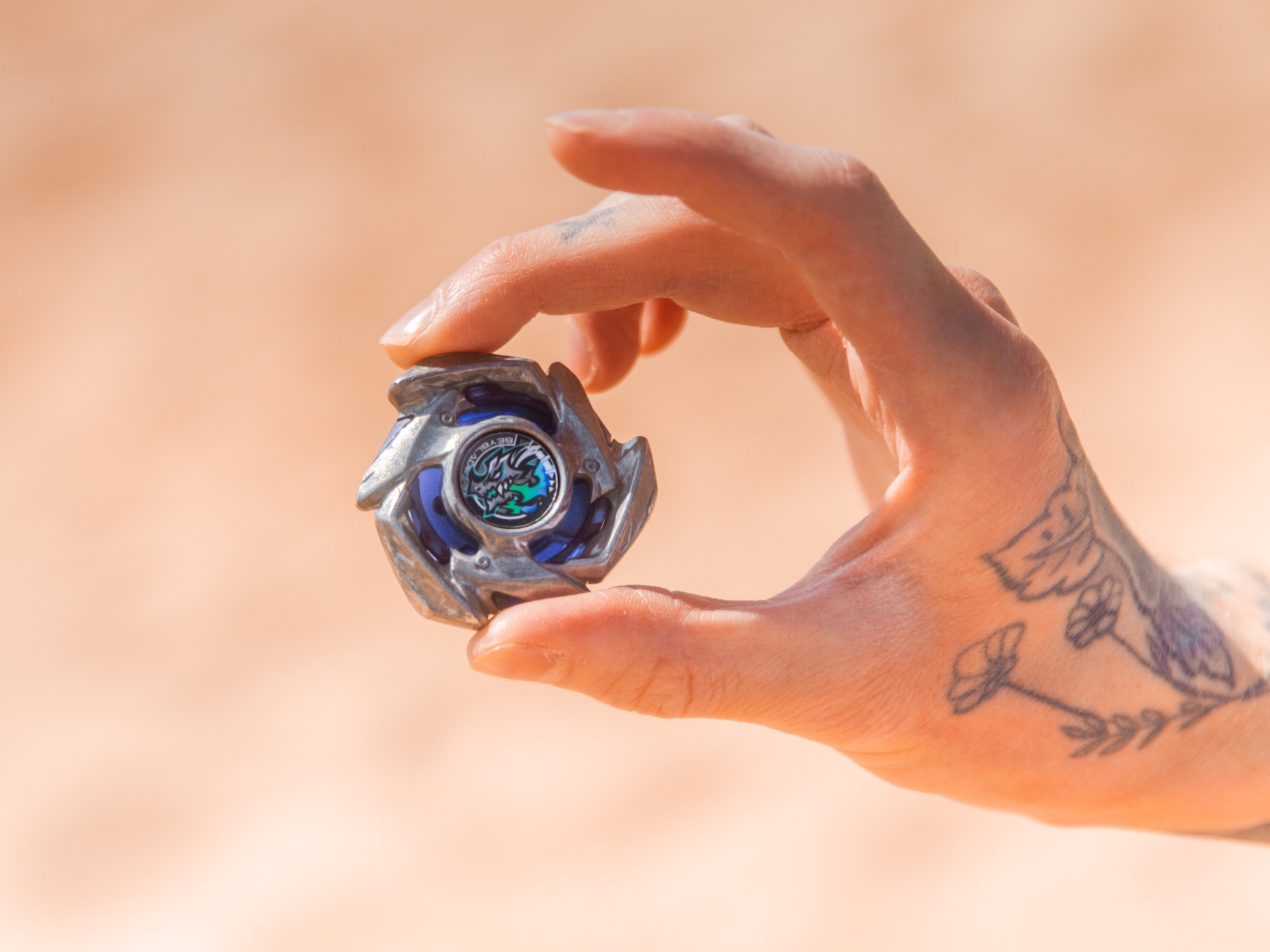 Beyblade Dranzer held up by tattooed hand, warm bokeh