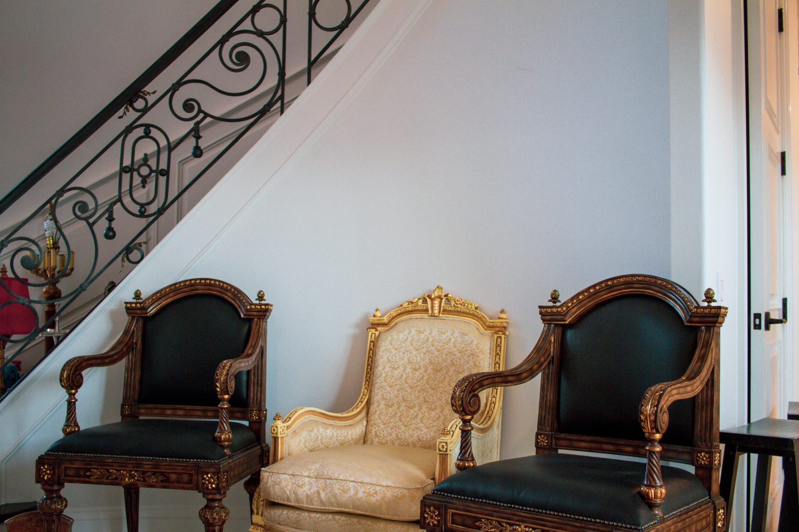 Three ornate French armchairs below wrought iron spiral staircase