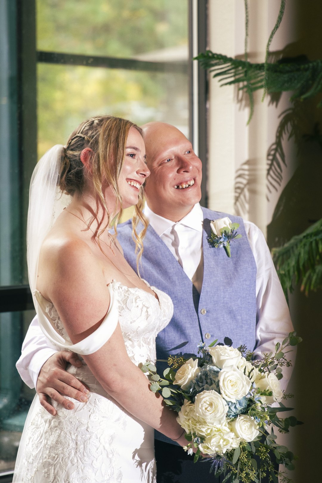 Bride and groom laughing together by a window, bride holding a white hydrangea bouquet