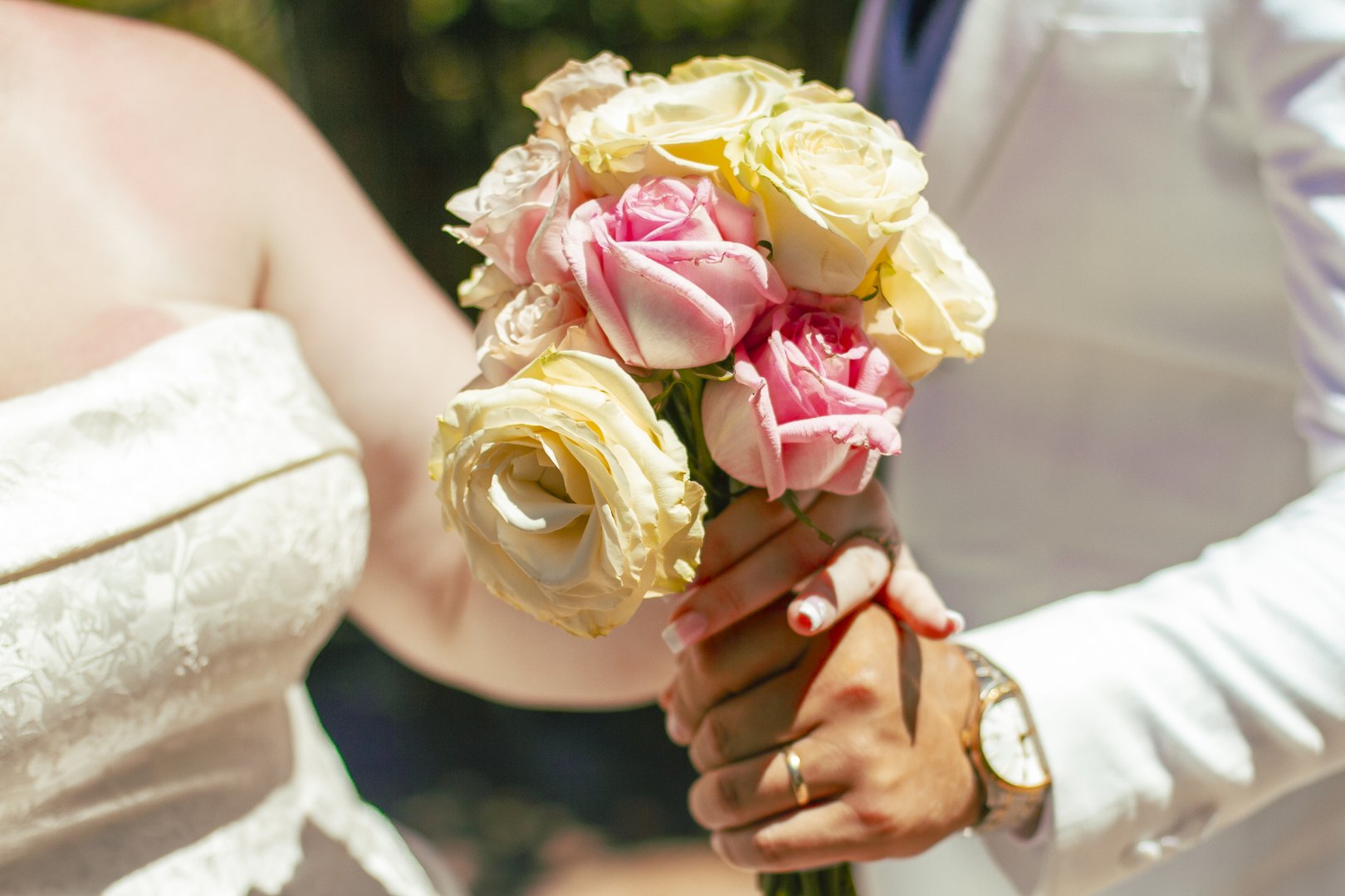 Bride and groom's hands holding a blush and cream rose bouquet