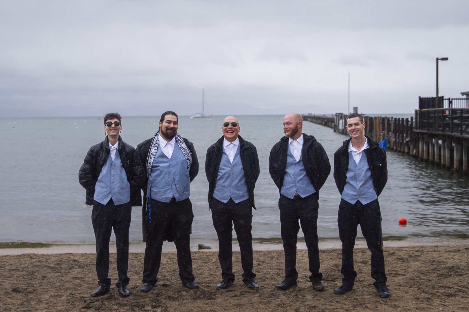 Groomsmen lined up on a lakeside beach under moody grey skies