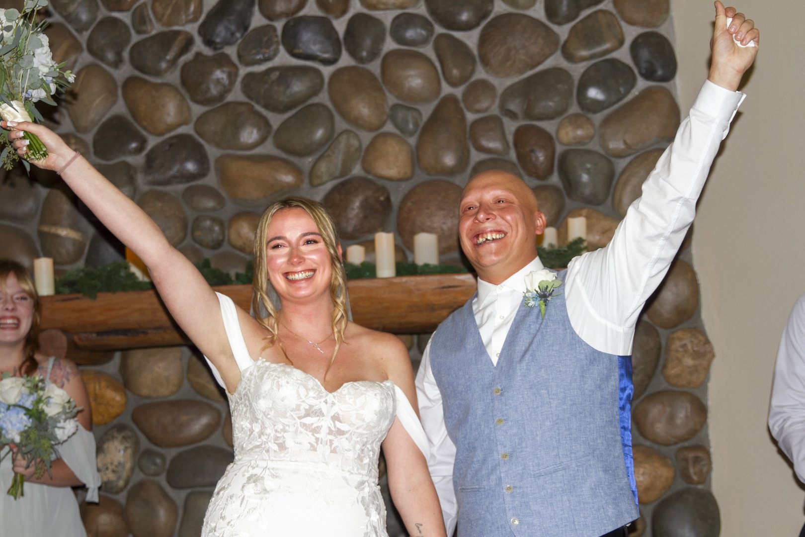 Bride and groom raise their arms in celebration in front of a stone fireplace