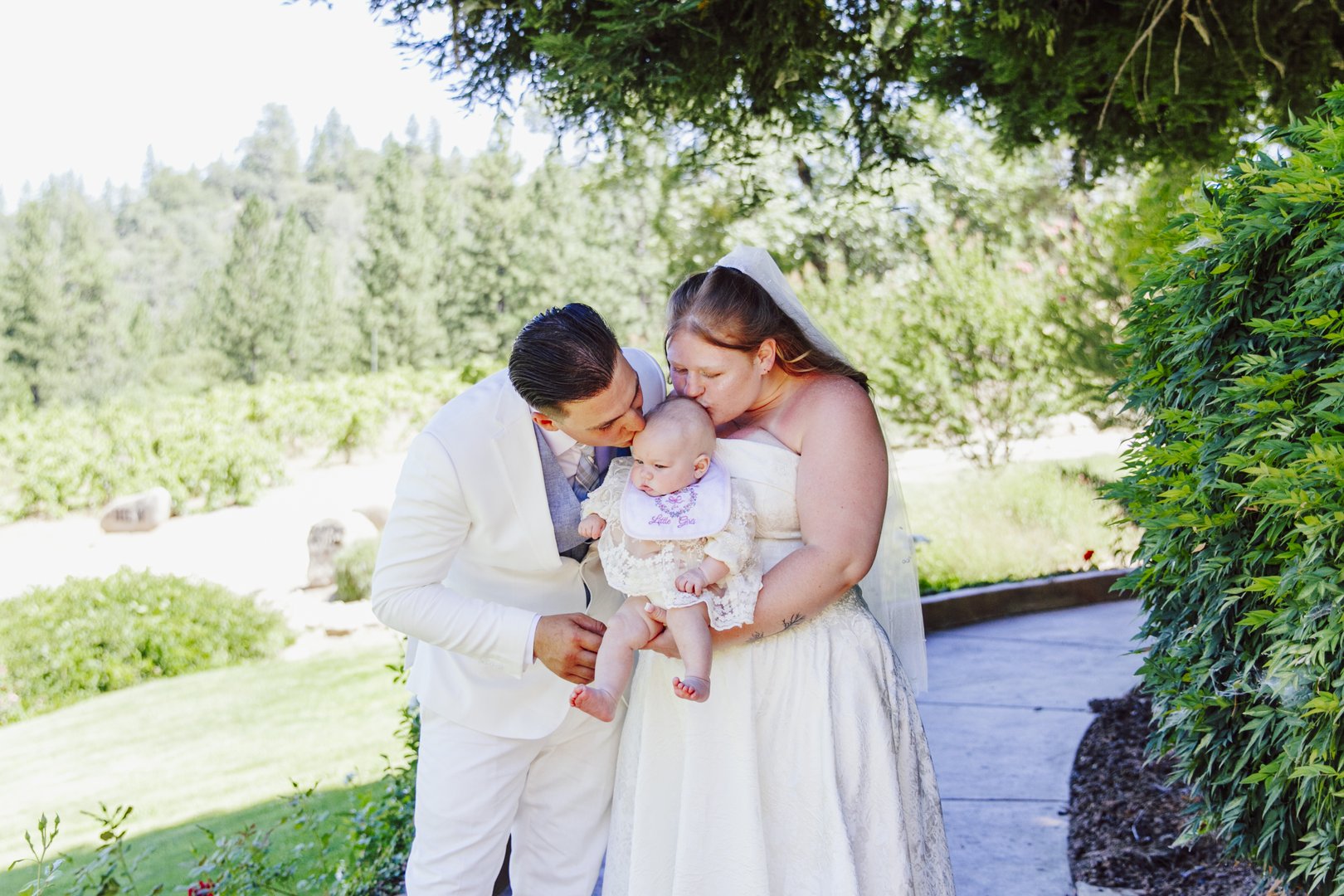 Groom kisses the bride as they hold their baby after the ceremony